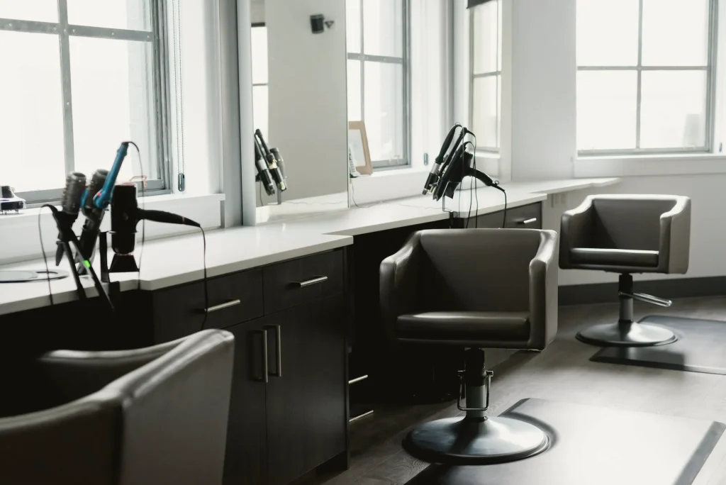 Salon mit Frisierplätzen, Sesseln und großen Fenstern